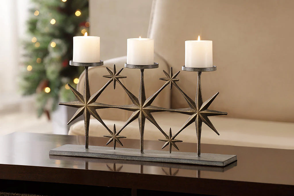 Decorative candle holder with three candles on a surface, with a Christmas tree in the background.