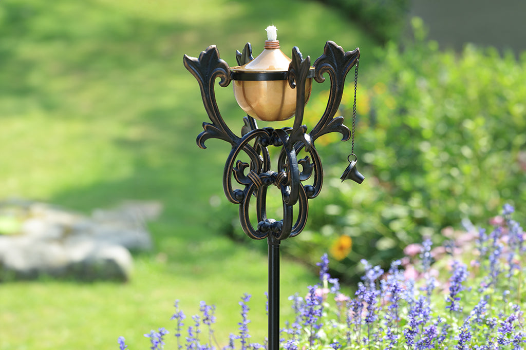 scrollwork encases the oil reservoir on a staked garden oil torch shown in a flower garden