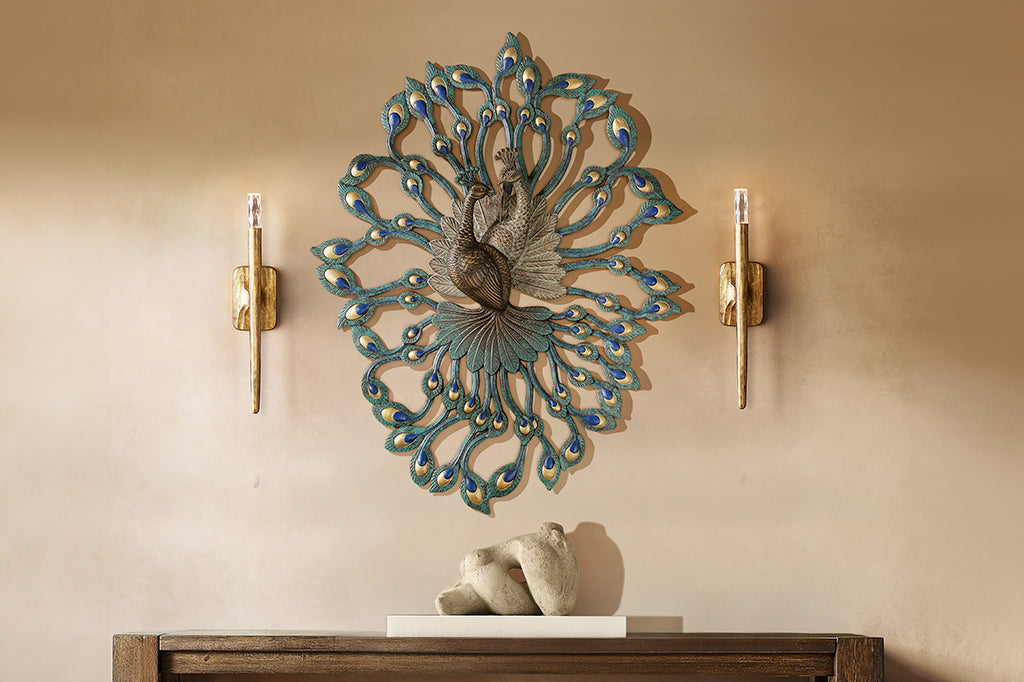 large peacock theme cast metal wall art showing two peacocks entertwined in 3D relief on a tan wall between torch sconces