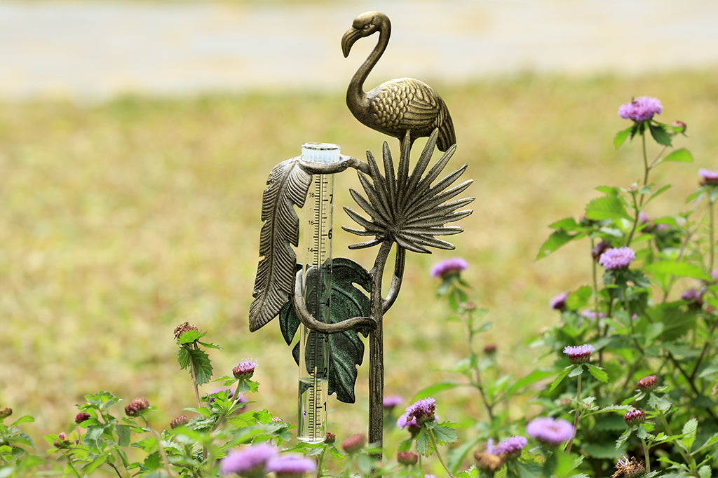 decorative garden rain catcher shows cast metal flamingo, and 3 tropical leaf accents in a floral garden