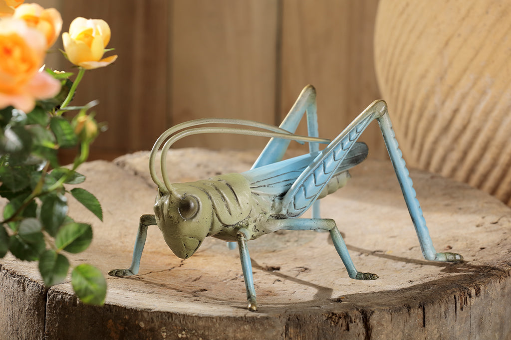 cast metal garden sculpture of grasshopper, shown on tree stump in a yard