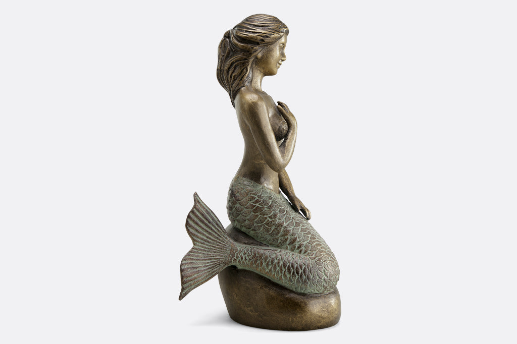Metal mermaid seated on a rock garden sculpture face right 