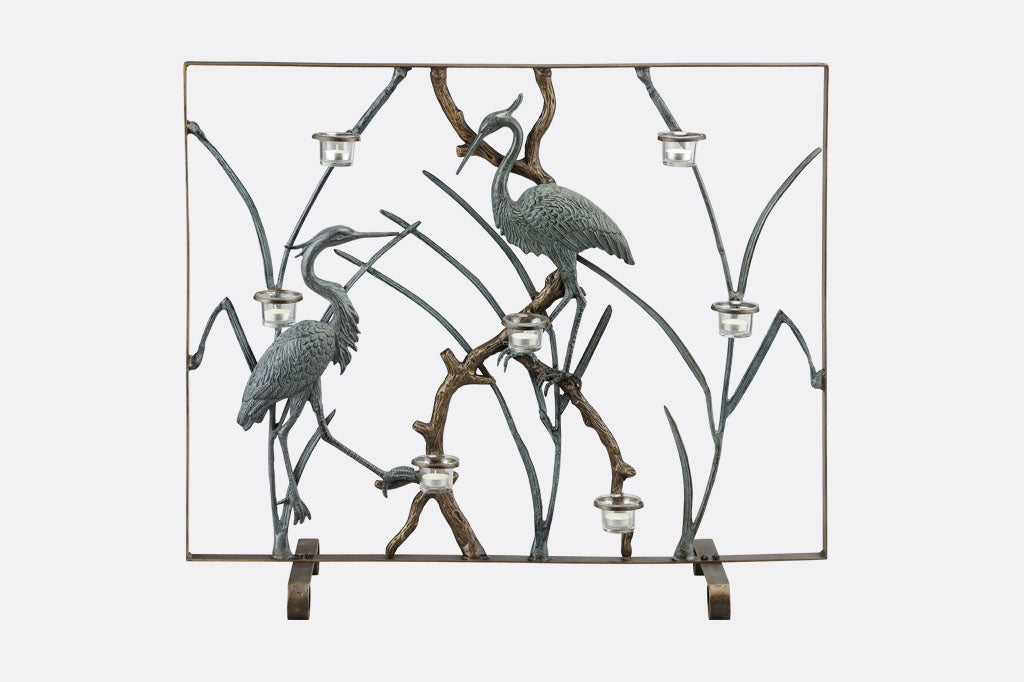 A firescreen of two Herons on branches with candleholders.
