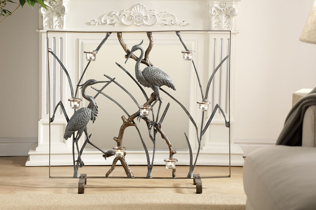 A firescreen with Herons and branches holding tealight candles in front of a fireplace.