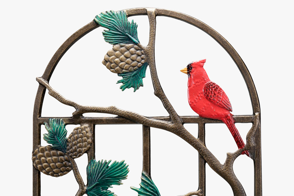 Closeup view of the top arch of a garden trellis featuring red cardinals, pine branches, and pine cones