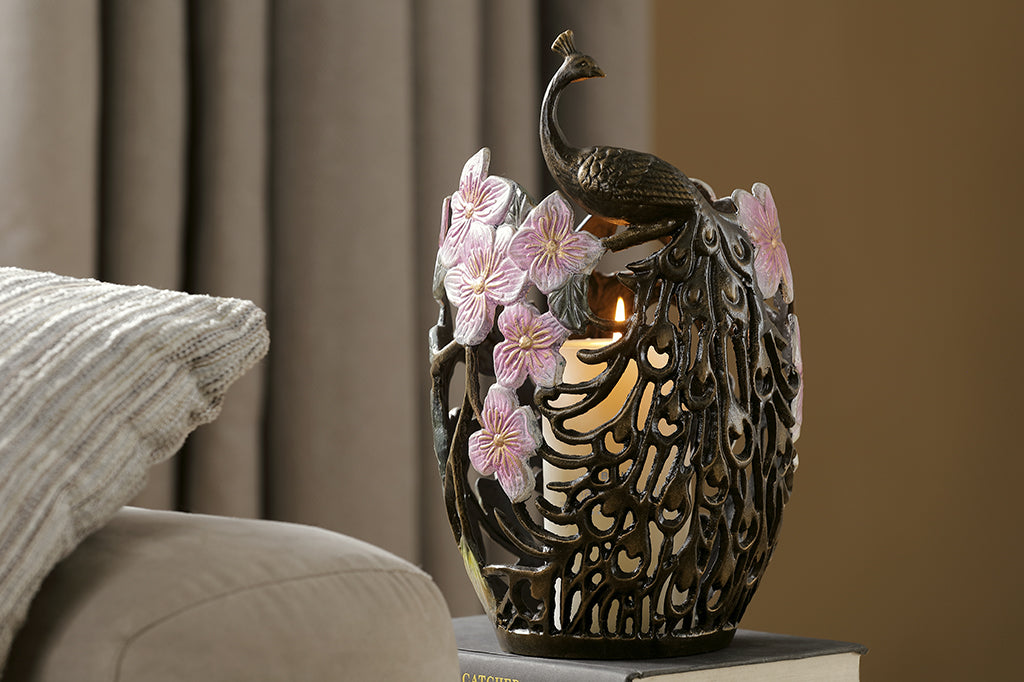 cast metal candleholder with peacock feathers and blossoms holding white pillar candle set beside couch 