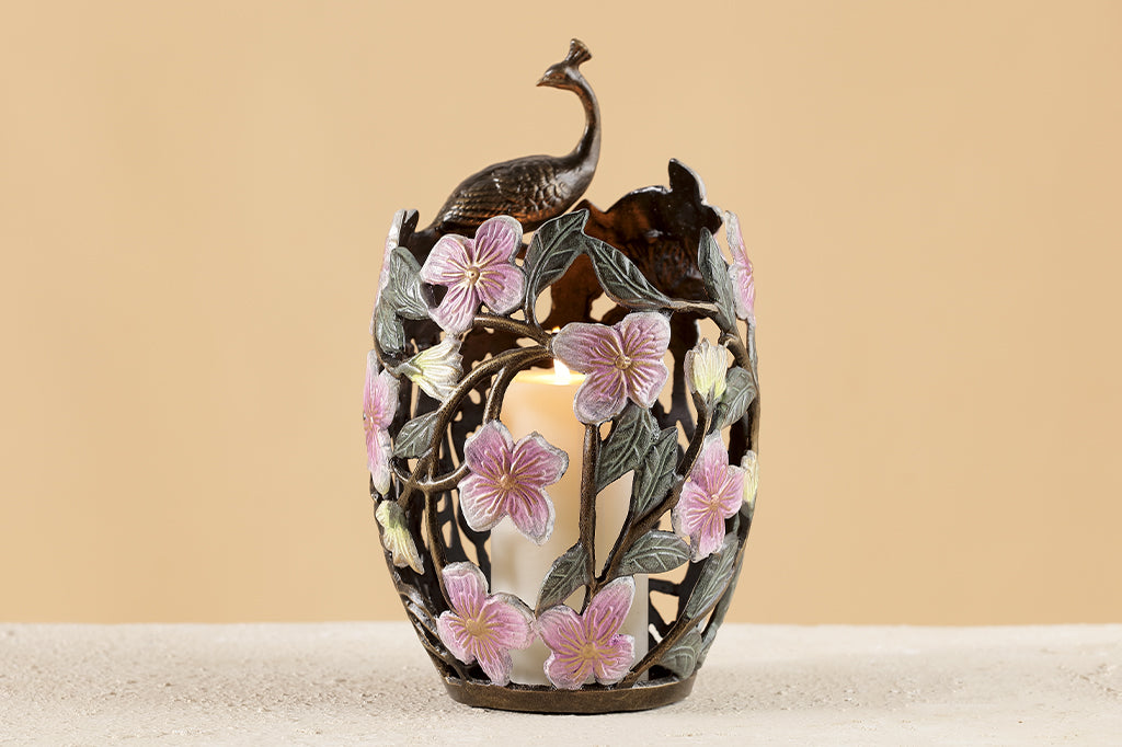 cast metal candleholder with peacock feathers and blossoms holding white pillar candle 