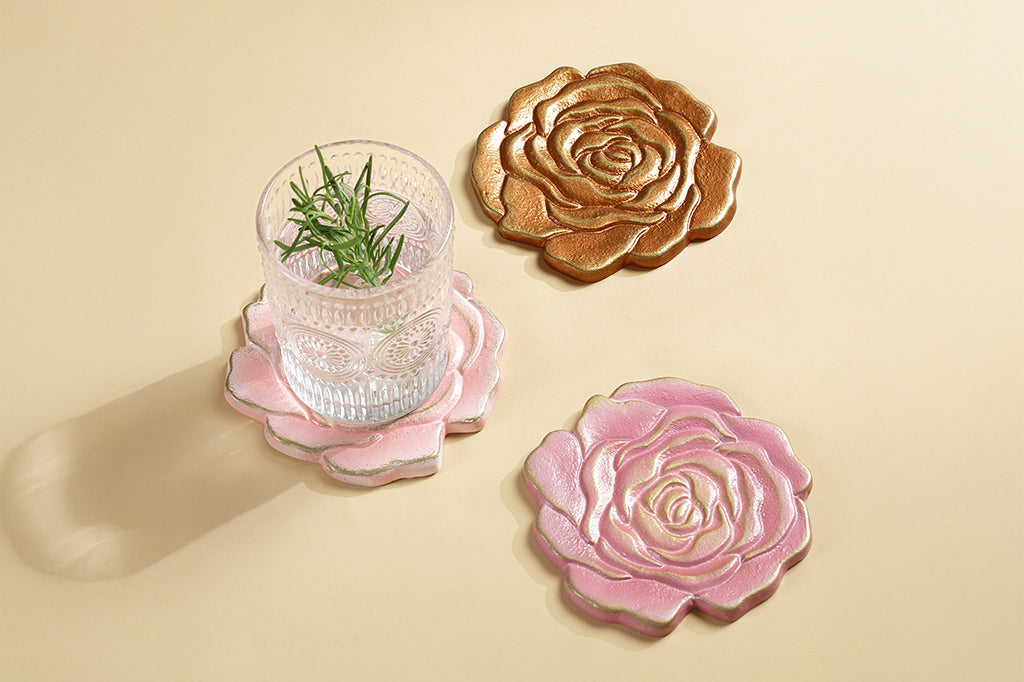 Three rose blossom coasters in shades of pink and copper, shown with glass of water