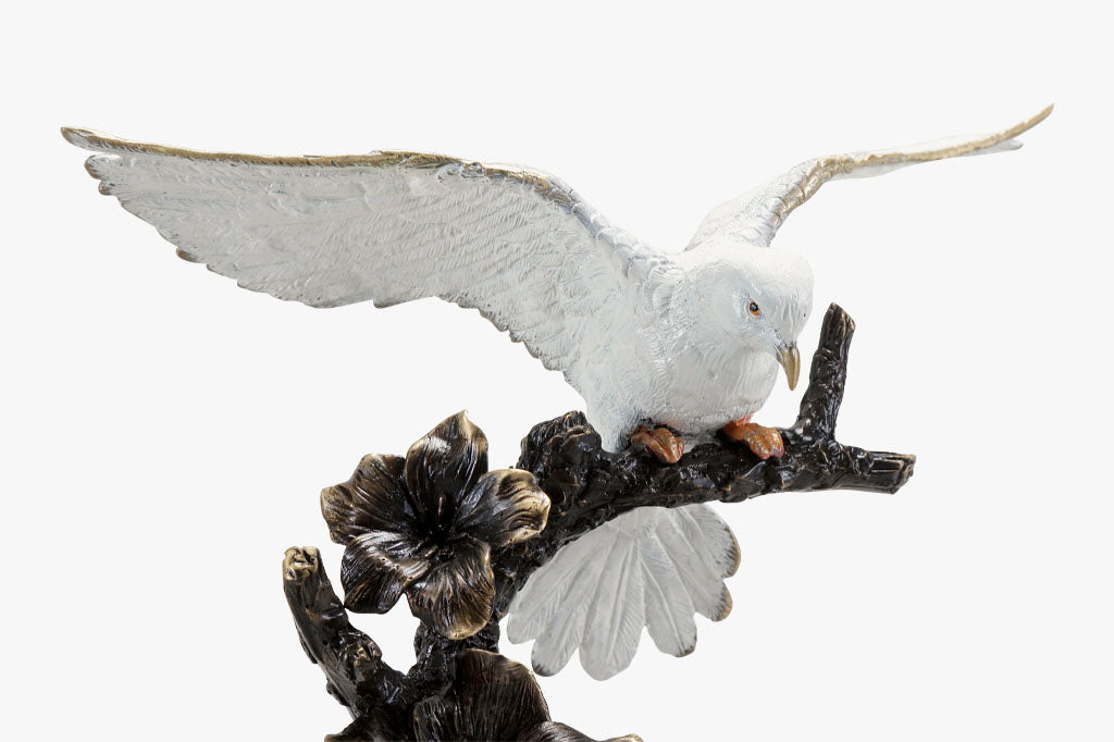 Close up view of brass sculpture of dove, with outstretched wings on a flowering branch