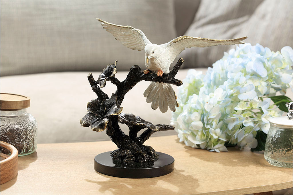 Brass sculpture of dove, with outstretched wings on a flowering branch shown on coffee table with jars and flowers