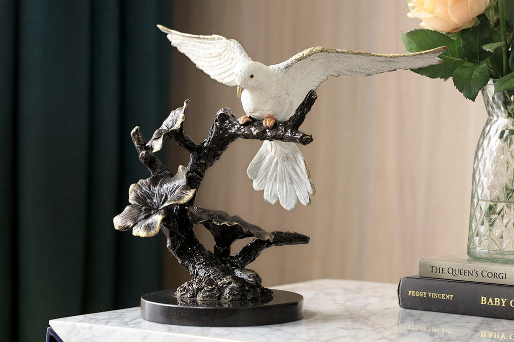 Brass sculpture of dove, with outstretched wings on a flowering branch shown of table with books in room