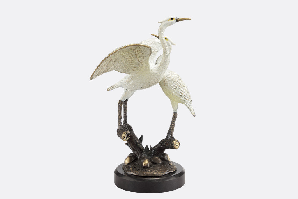 Statue of two cranes on a branch with a white background