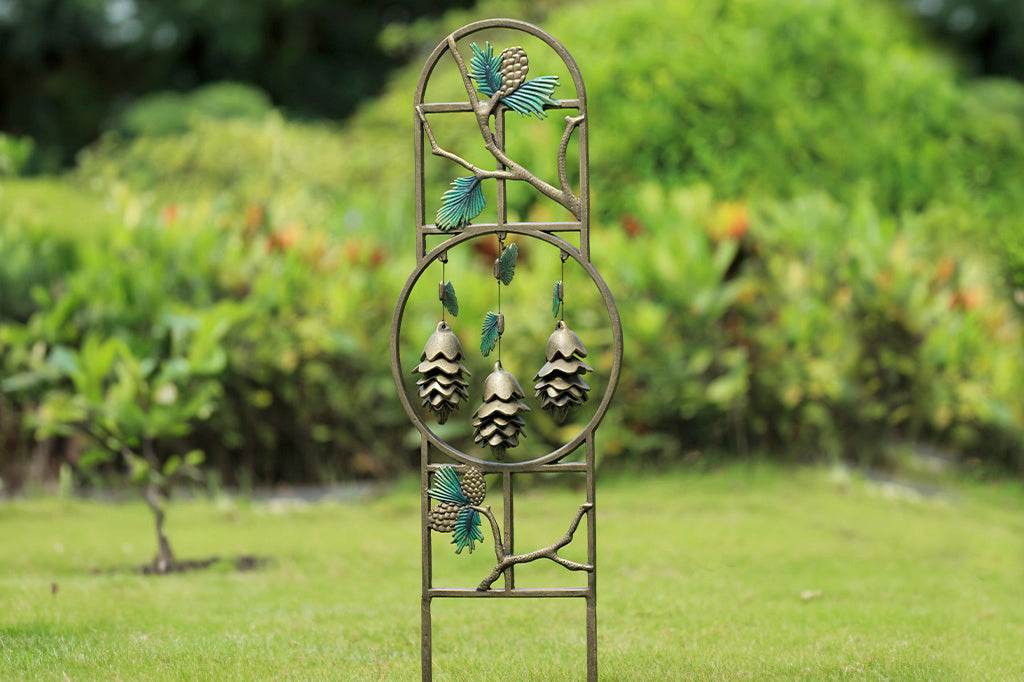 Pinetree theme garden trellis with 3 pinecone shaped pendants hanging within sculptural hoop. Trellis is shown in grass in outdoor scene.