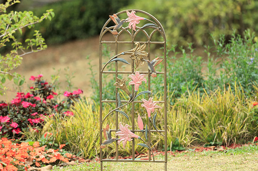 arched trellis featuring pink and gold lilies with sculpted hummingbirds at 3 blossoms. Shown in landscaped yard
