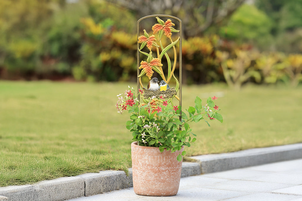 cast metal birds nest planter trellis placed in terracotta planter with red flowers placed on garden road 