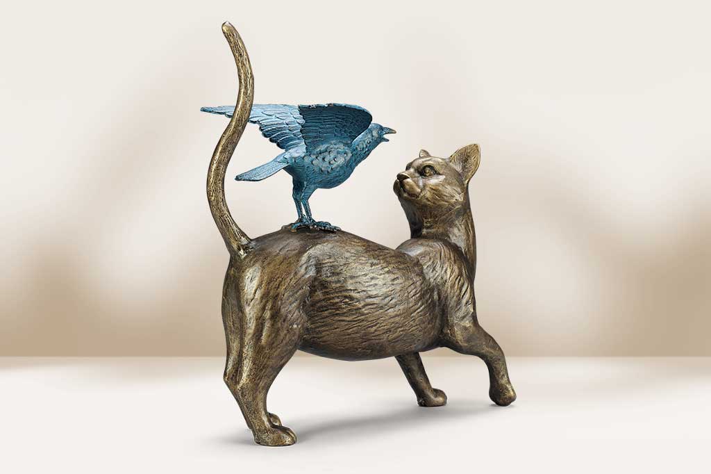 Bronze sculpture of a cat with a bird on its back against a beige background