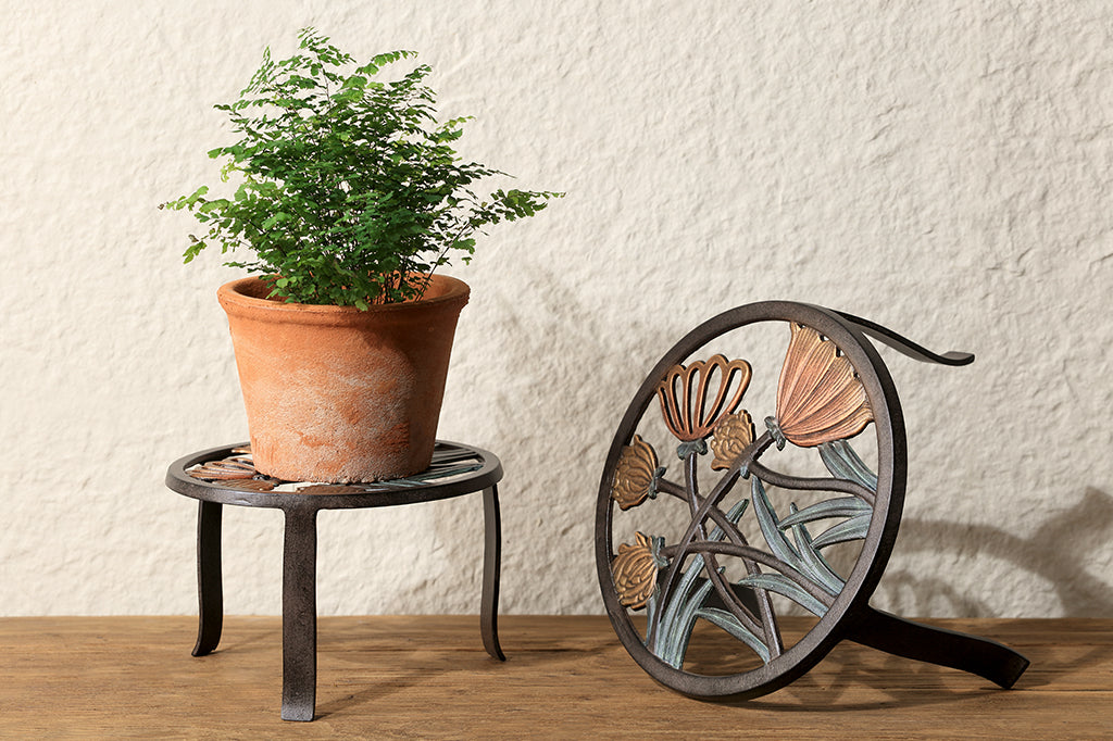 two plant stands shown with potted plant, one is tipped to reveal the clover blossom motif