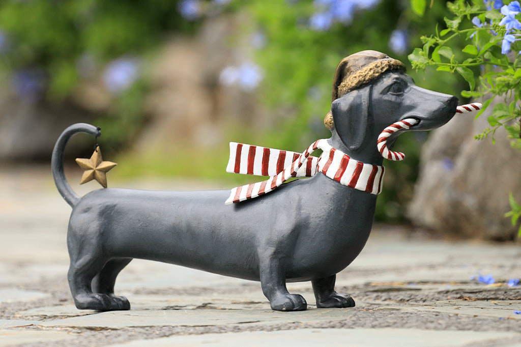 Cast metal holiday dachshund holding candy cane in mouth and wearing a santa hat along with striped scarf 