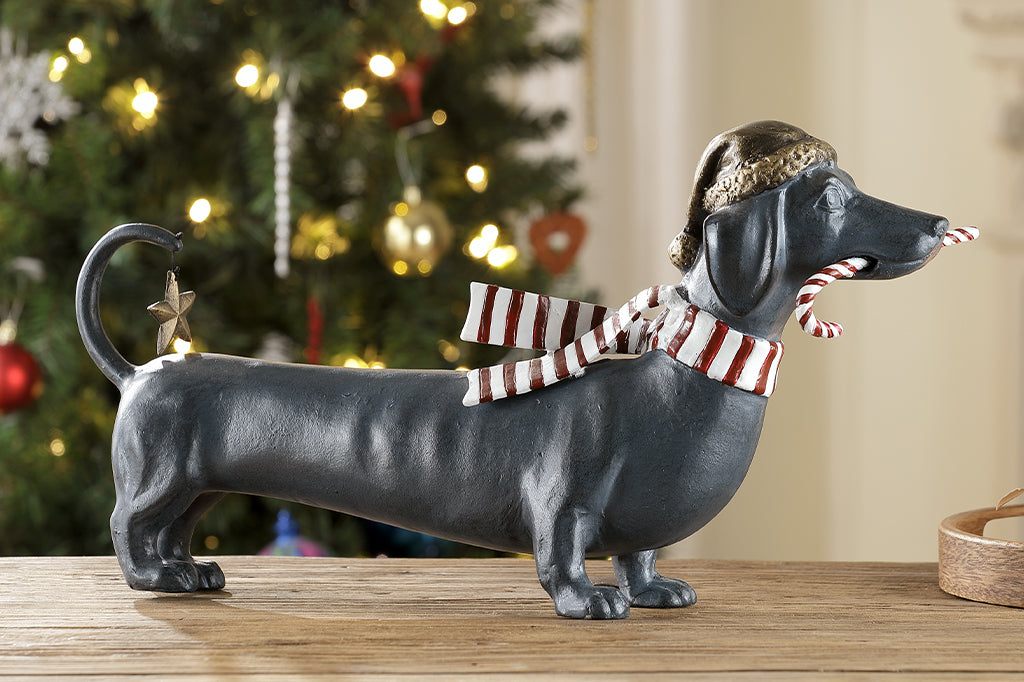 Cast metal holiday dachshund holding candy cane in mouth and wearing a santa hat along with striped scarf 