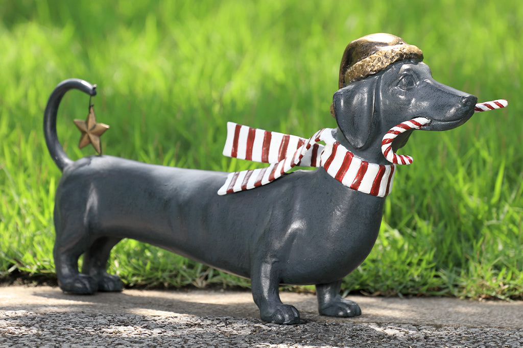 Cast metal holiday dachshund holding candy cane in mouth and wearing a santa hat along with striped scarf 