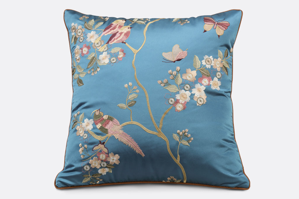 dark blue satin pillow with embroidered flowers, birds, branches, and fluttering butterflies