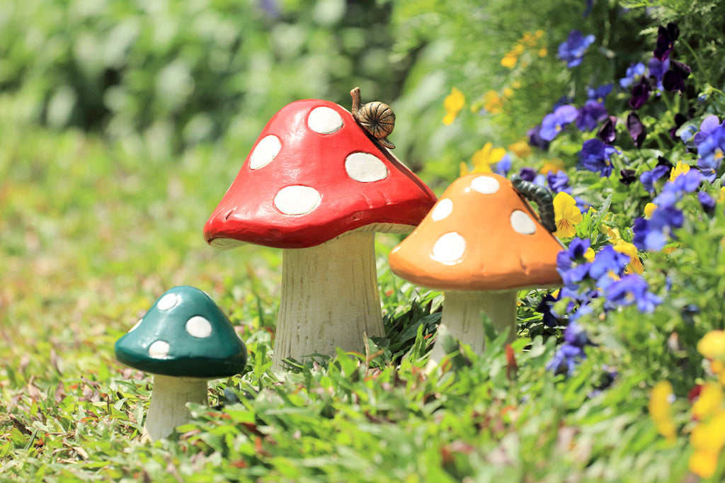 set of three fantasy mushroom garden sculpture in garden bed with purple blooms