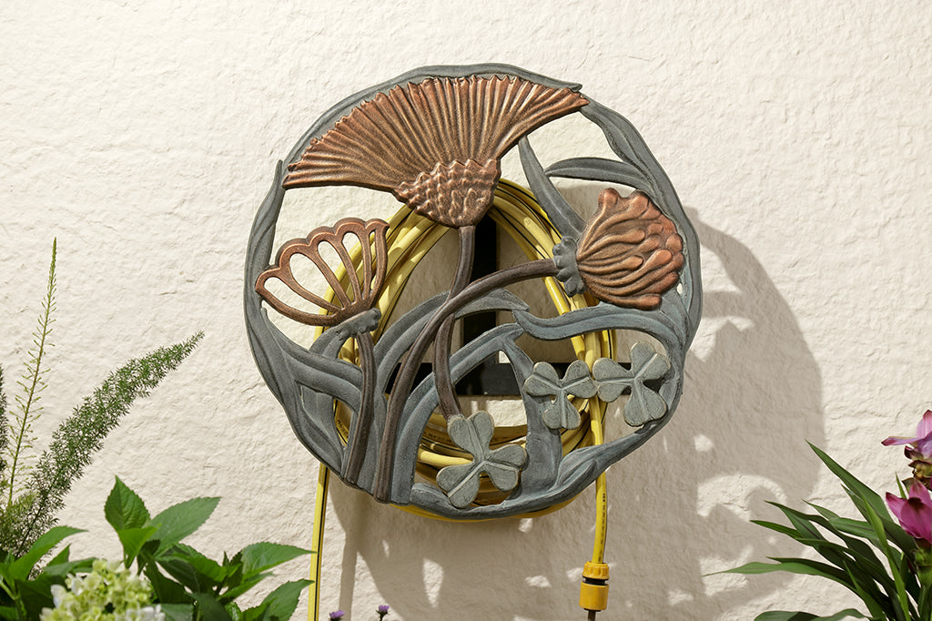 garden hose holder with clover flower and leaf detailing shown on wall above plants