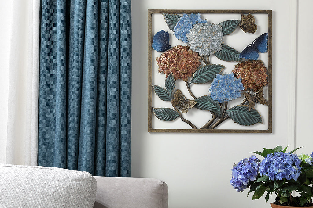 Wall plaque features hydrangea blossoms, butterflies and green leaves. Shown in living room with potted hydrangeas and blue curtains