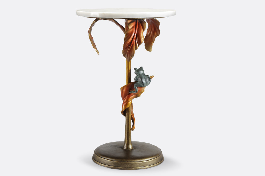 cast metal tropical drink table with white marble top in a coppery color featuring tropical leaves and a green frog balancing on a leaf 