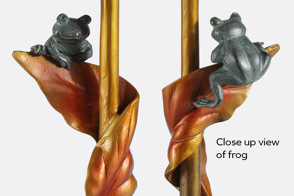 close up view of sculpted green frog balancing on a copper colored leaf on a drink table