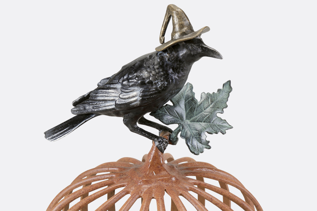 Detailed view of the black raven holding a green leaf in talon with witch hat