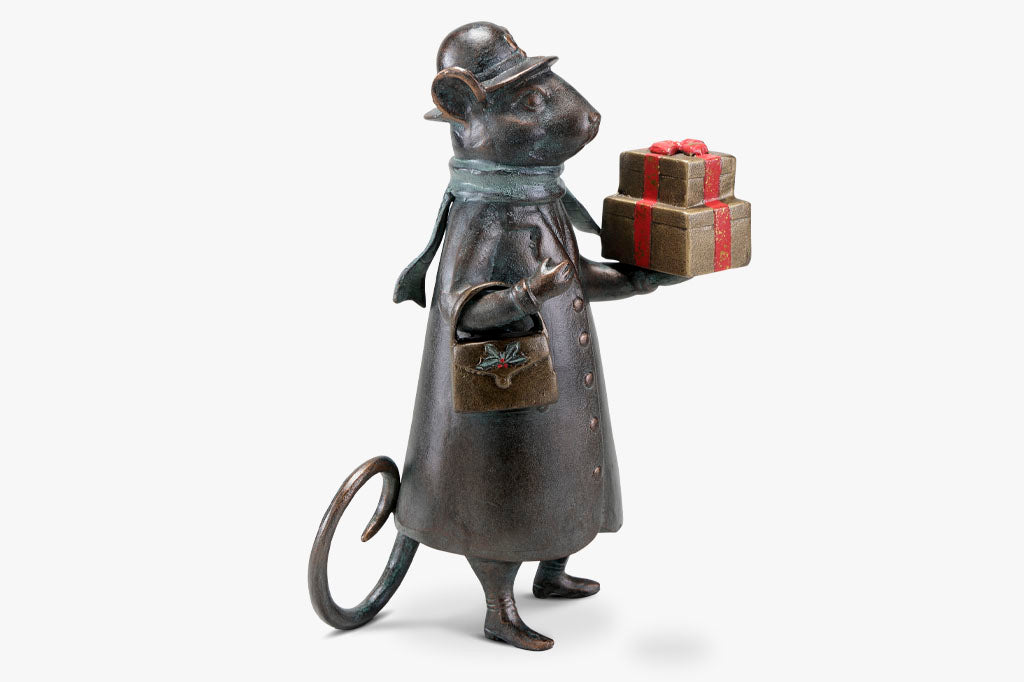 Holiday metal sculpture shows a mouse dressed in wintercoat with purse holds 2 gold and red wrapped gifts in paw; she wears a green scarf and a hat with bow on it.