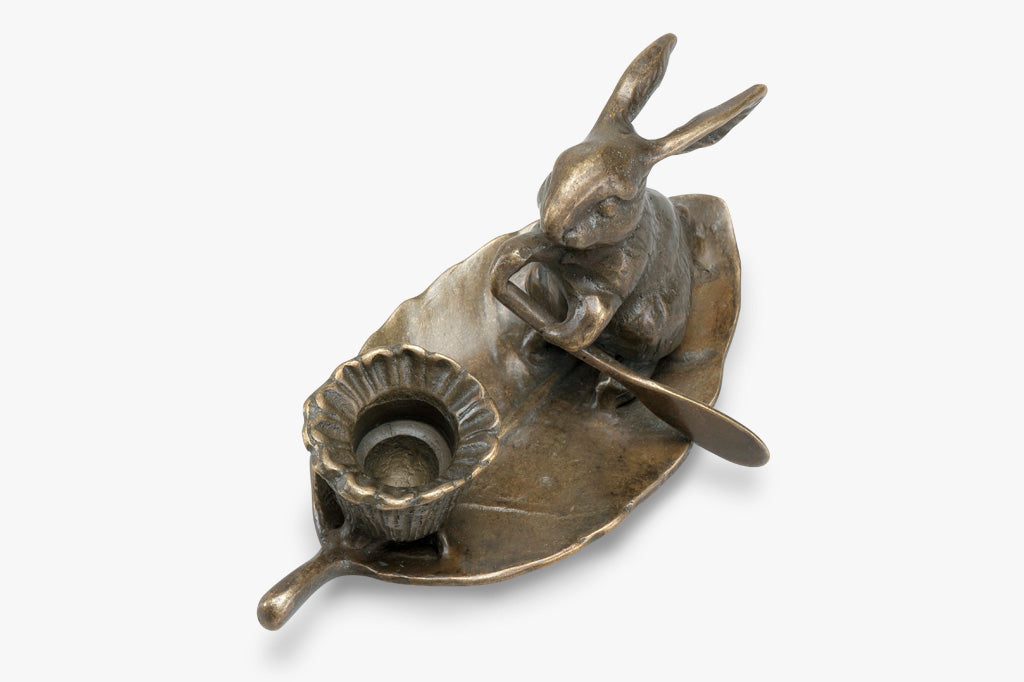 taper candleholder in brass; rabbit rowing a leaf with a blossom-shaped candleholder cup