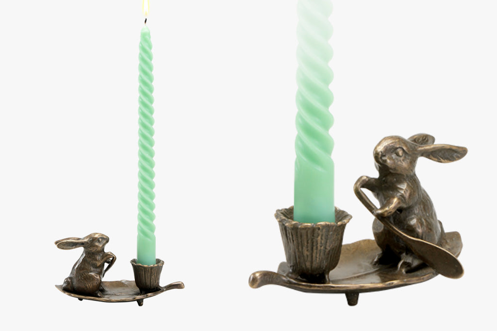 face left and face right view of a small candleholder of rabbit rowing a leaf with a blossom-shaped candleholder cup; holds green taper candle