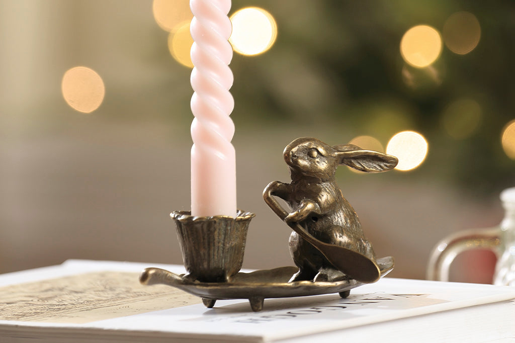 taper candleholder in brass; rabbit rowing a leaf with a blossom-shaped candleholder cup in a christmas scene; holding a pink candle