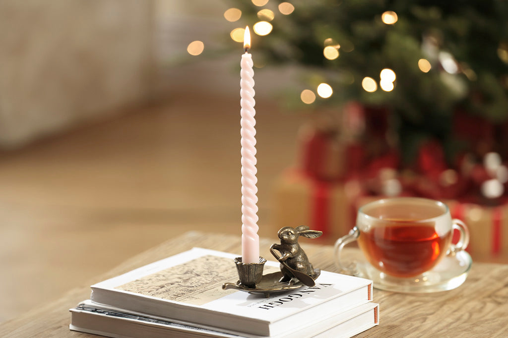 taper candleholder in brass; rabbit rowing a leaf with a blossom-shaped candleholder cup in a christmas scene; holding a pink taper candle