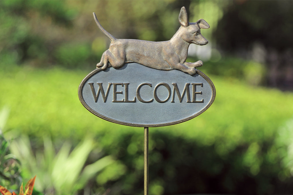 cast metal Dachshund welcome sign set in garden bed. Leaping Dachshund over the words welcome 