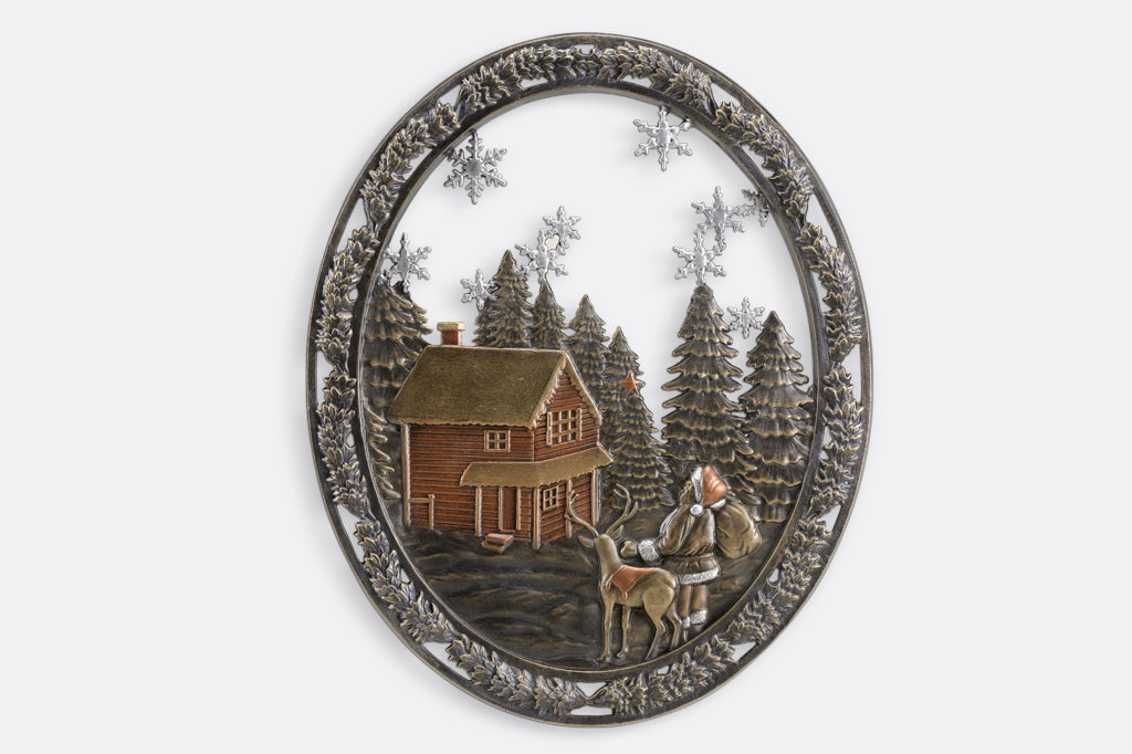 Cast metal circle wall art with pine trees, a cozy cabin, and santa with a present sack 