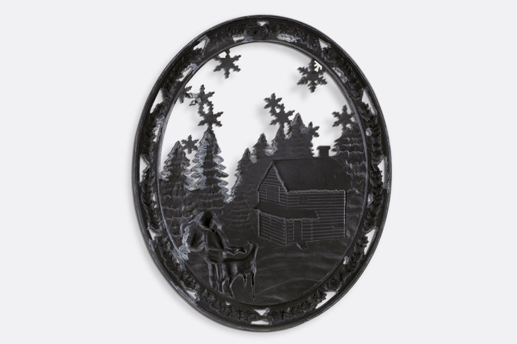 Cast metal circle wall art with pine trees, a cozy cabin, and santa with a present sack back