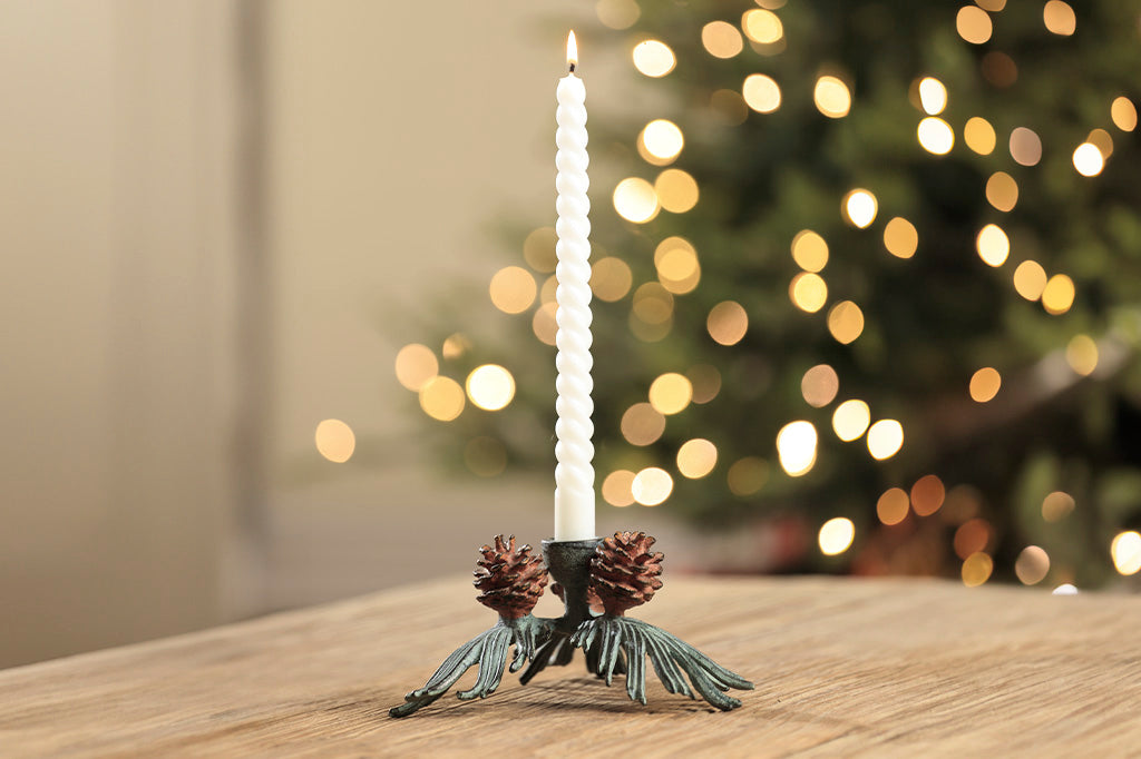 taper candle holder shaped like pineneedle cluster with 3 pinecones shown in front of Christmas tree