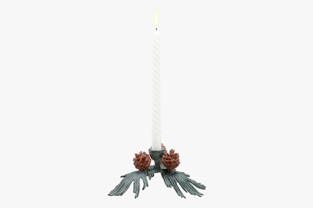 side view of taper candle holder shaped like pineneedle cluster with 3 pinecones shown holding 1 lit, white taper candle