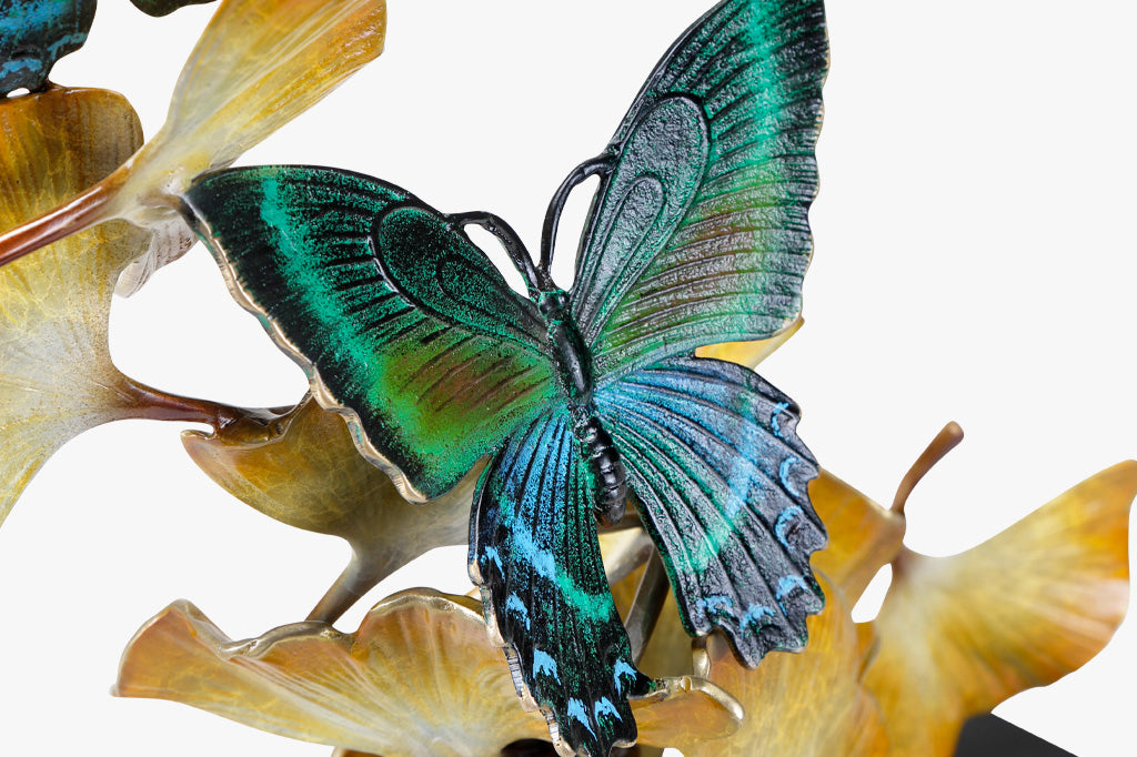 Close up view of blue, green, and black butterfly wings on sculpture of gingko leaves 