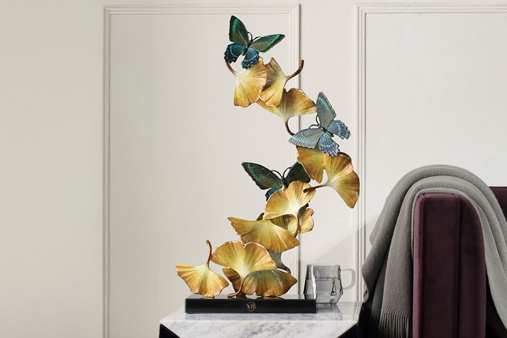 Limited Edition sculpture features fluttering ginkgo leaves and exquisitely finished butterflies, spiraling upwards from a marble base. Shown on side table in room next to a couch, glass of water for scale