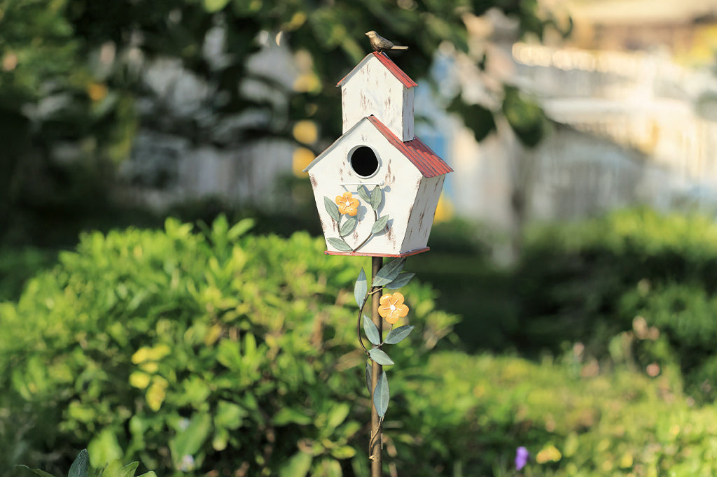 Decorative Iron birdhouse on stake, looks like rustic barn, accented with vining flowers and bird on roof