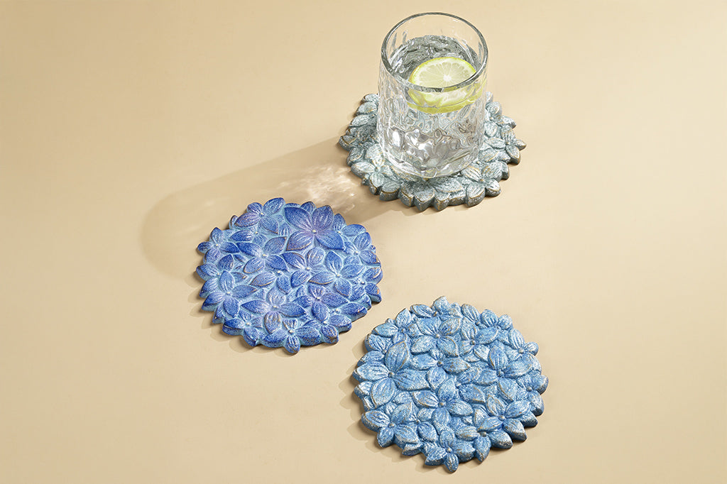 3 coasters of blue hydrangea blossoms shown with glass of lemon water