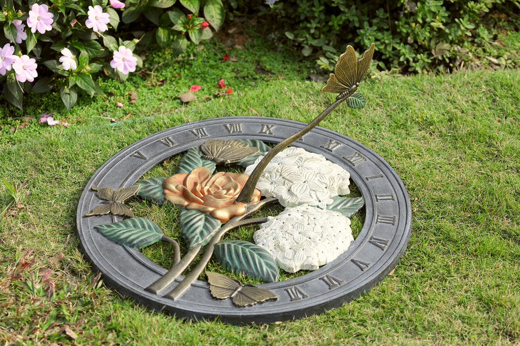 Shown on grass, a Sundial in cast metal with roman numerals, and a butterfly on the shadow-casting gnomon. Features butterflies, hydrangea, and roses.