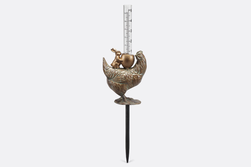 cast metal chicken with bunny holding a cracked egg holding a glass rain gauge face left