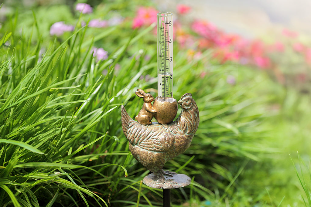 cast metal chicken with bunny and cracked egg with rain gauge, set in garden bed  