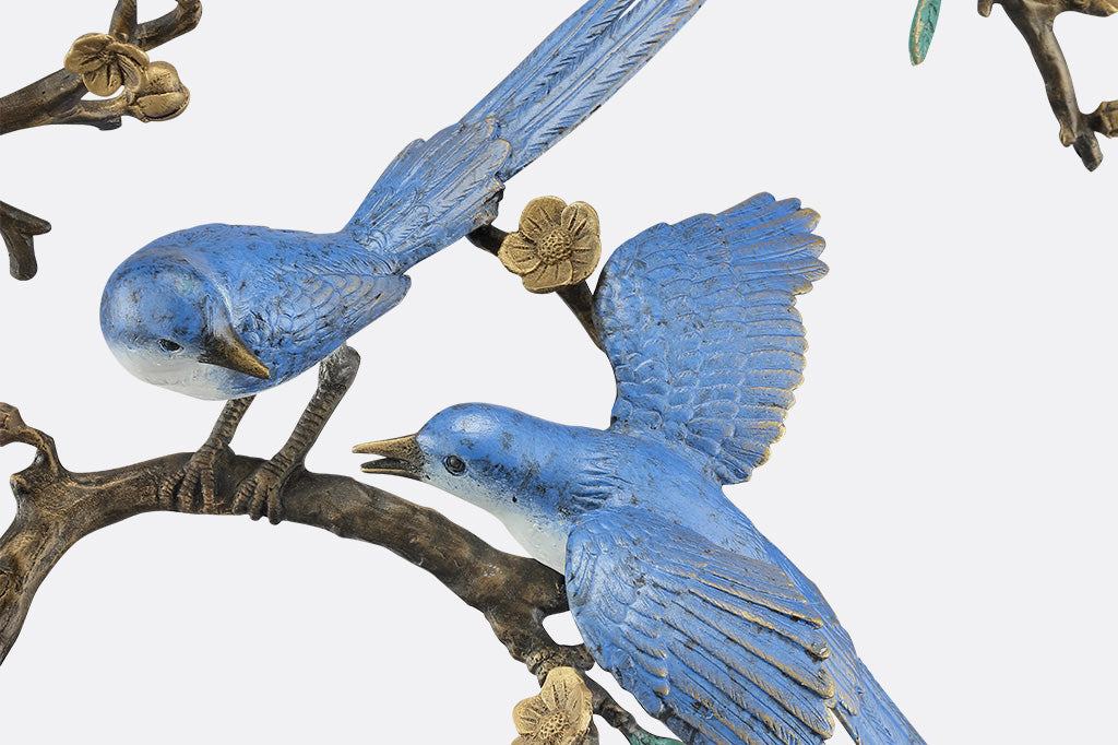 A close up of a statue of two blue songbirds perched serenely on a circular branch.