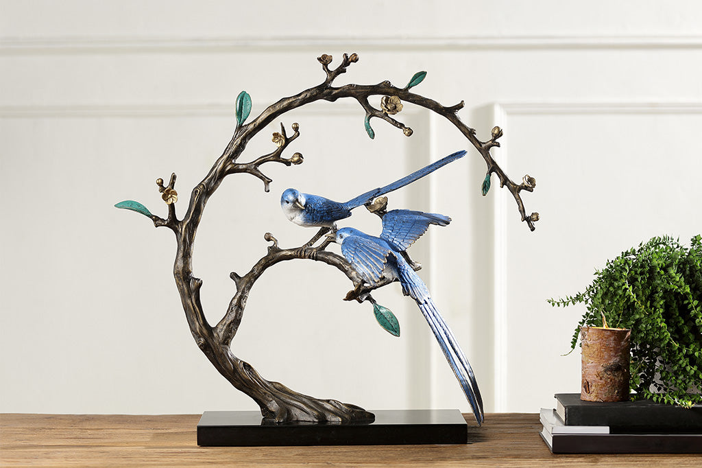 A statue of two blue songbirds perched serenely on a circular branch placed upon a table.